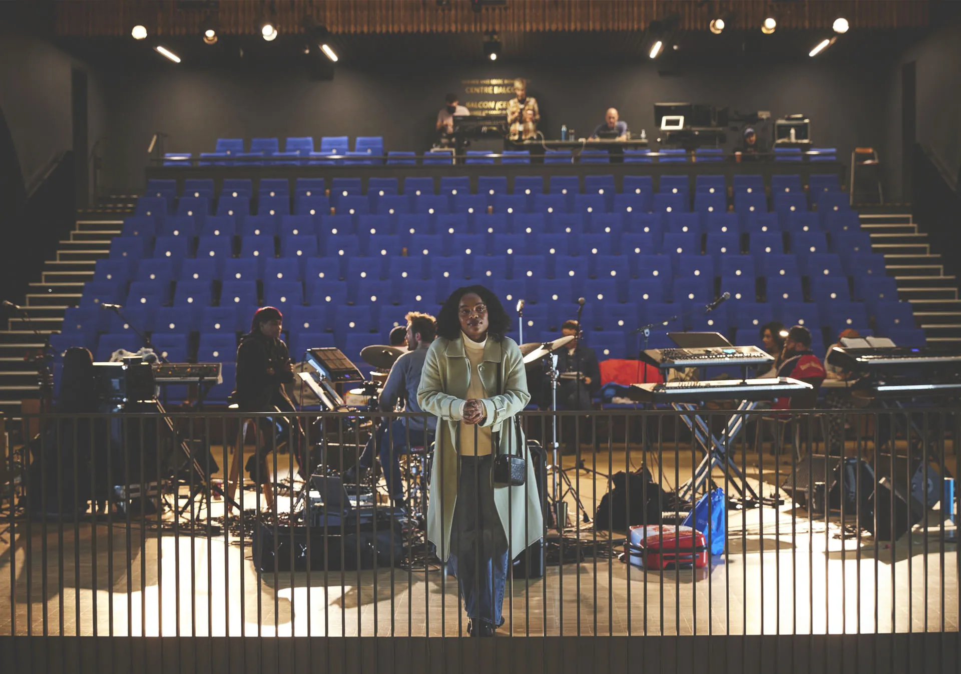Woman in the foreground as a band sets up to perform in the performance hall of Studio Bell