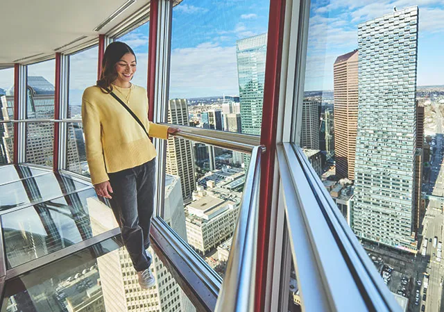 woman standing on the Calgary Tower observation deck with the eye-level upper skyline behind her