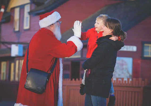 a mother holds a young child as he high fives Santa Claus at Heritage Park