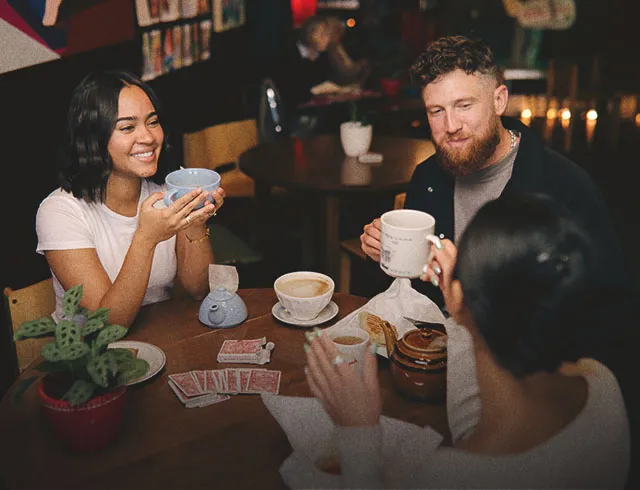 friends sipping tea and coffee while playing cards at a table at Congress Coffee