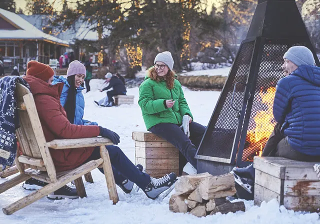 group of friends warms up by a wood fire pit on Bowness Lagoon after skating