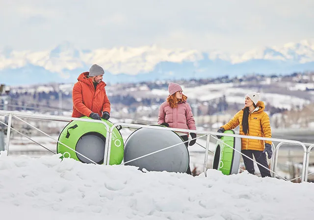 three friends riding the conveyer up WinSport snow hill with snow tubes