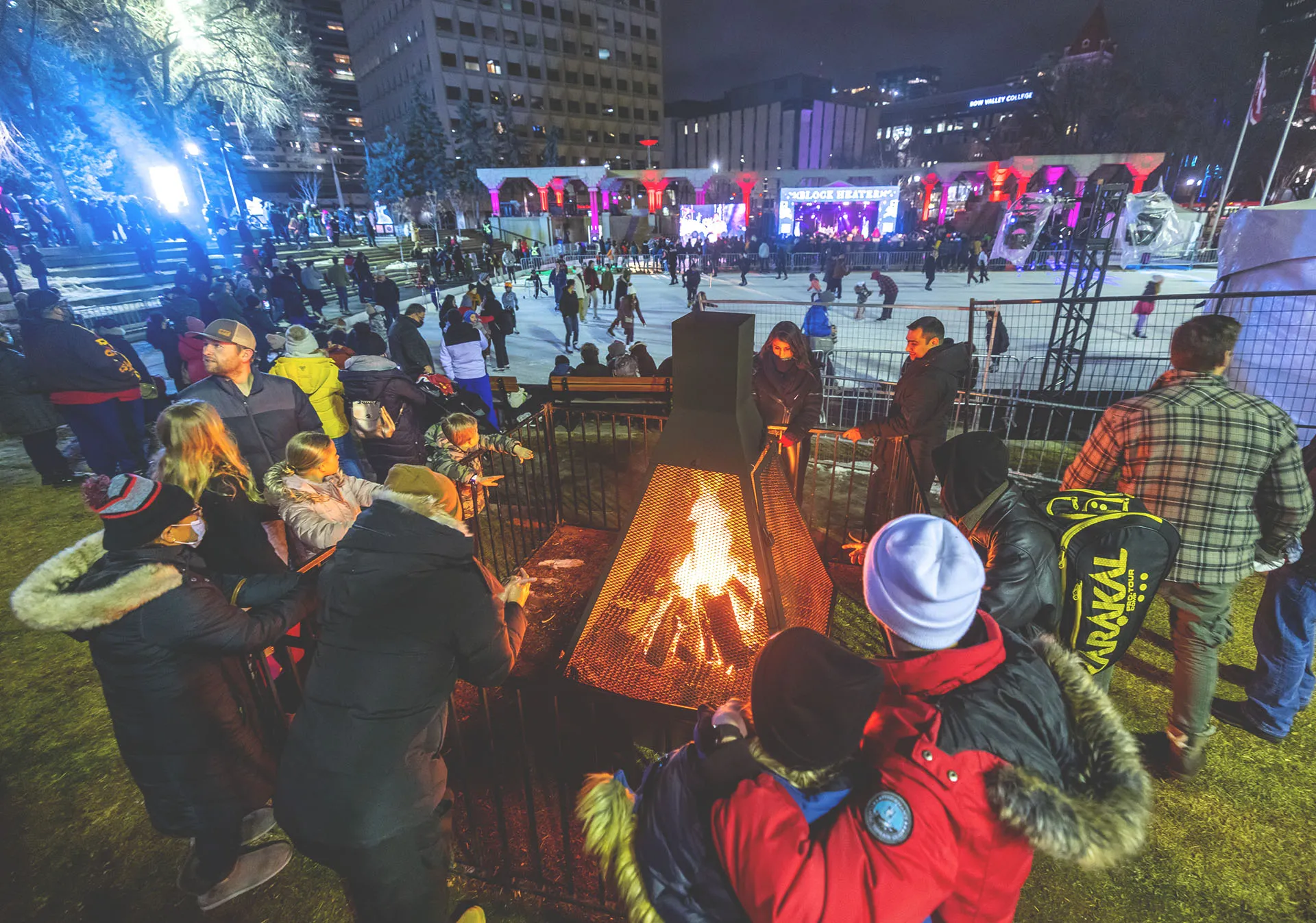 groups of people enjoy skating, warming up by a fire pit, and live music during Block Heater in Olympic Plaza
