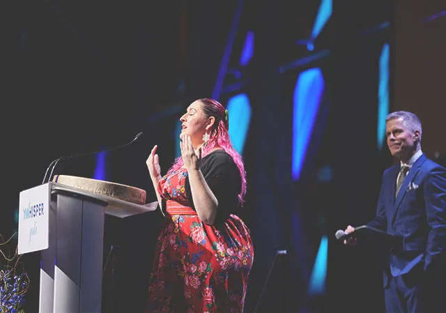 An indigenous woman giving a blessing in front of a podium during a gala convention