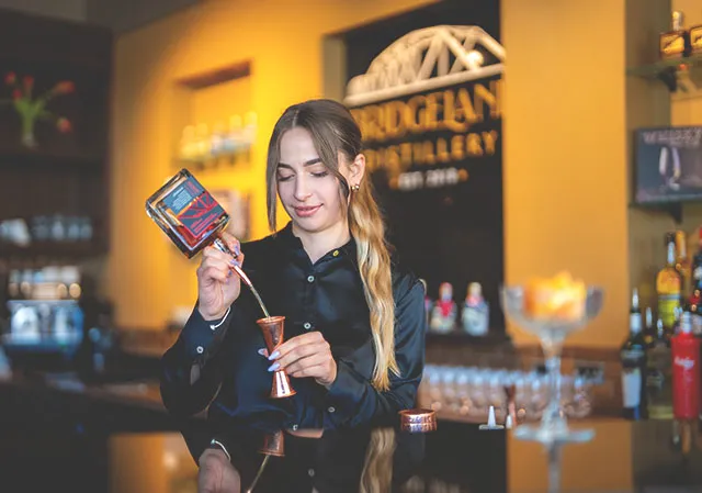 a bartender pours alcohol from a bottle into a bar measure at Bridgeland Distillery