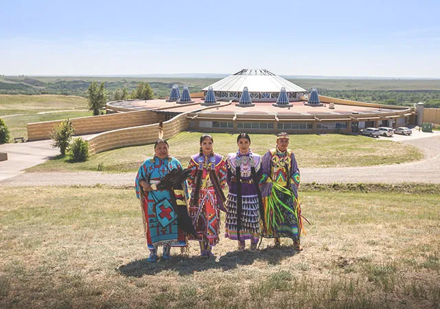 Siksika Blackfoot dancers standing in front of the Blackfoot Crossing Historical Park Interpretive Centre