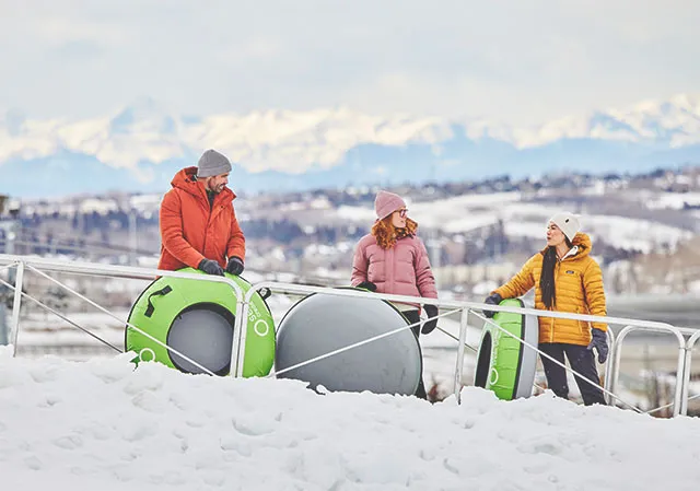 three friends riding uphill at WinSport to snow tube