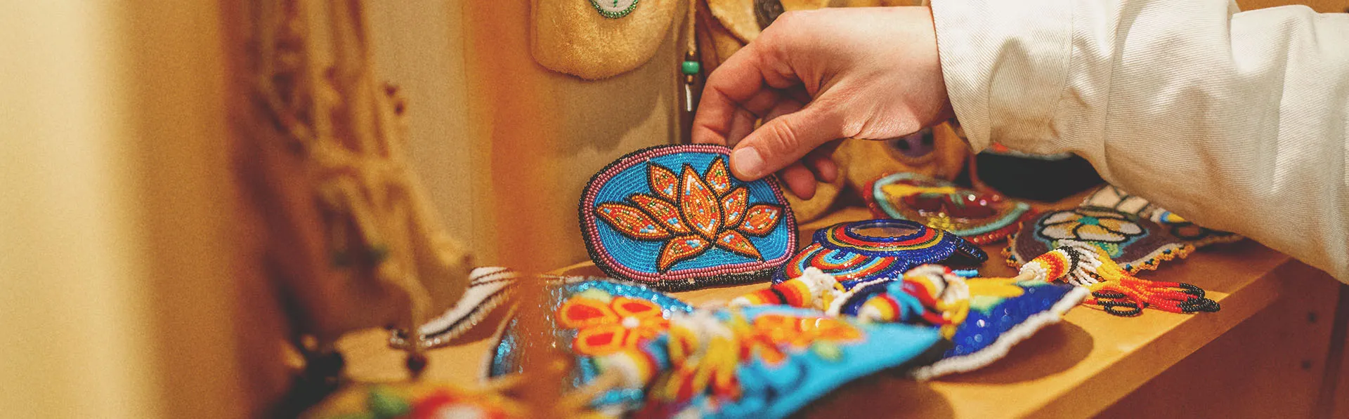 Someone picks up a Beaded Orange Flower Barrette from a shelf full of other beadwork arts and crafts as well as ceremonial and medicine bags