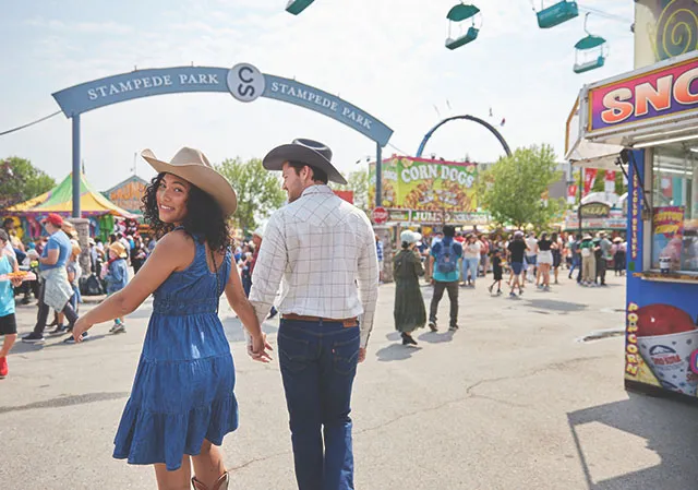 couple in western wear holding hands and walking through the midway grounds at the Calgary Stampede