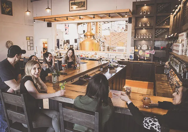 a group sits at the bar socializing in the tasting room at Two Rivers Distillery