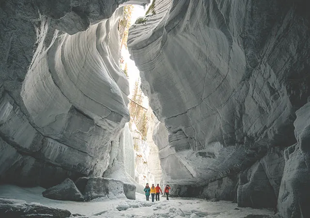 A distant shot of a group touring Maligne Canyon, surrounded by cool canyon formations, while ice walking and hiking in Jasper National Park