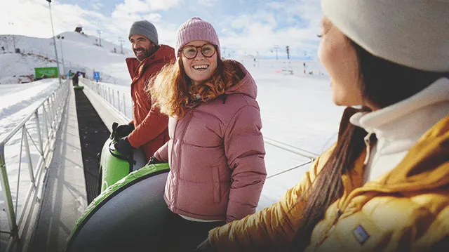 three friends riding the conveyer up WinSport snow hill with snow tubes