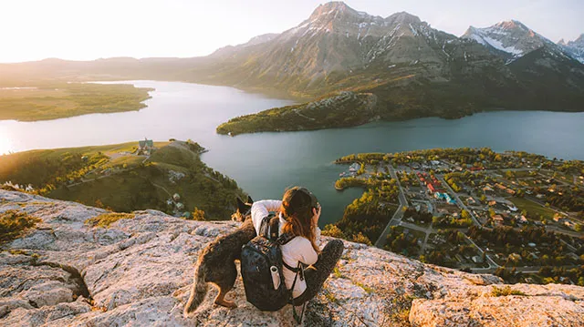 Scenic shot of woman and a dog sitting on rocks /hiking and taking a picture of the water and mountains in the distance