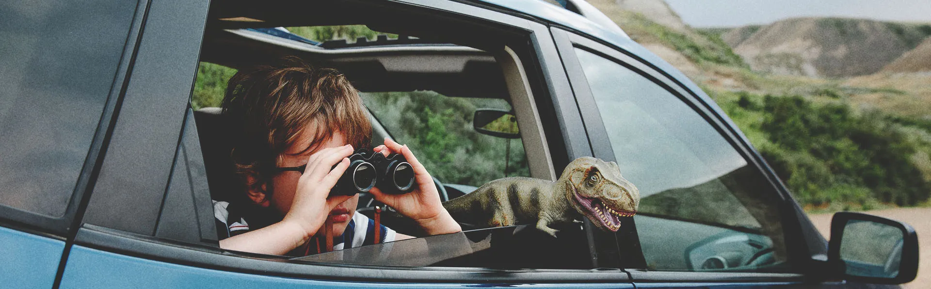 Kid looking outside through binoculars from a car.